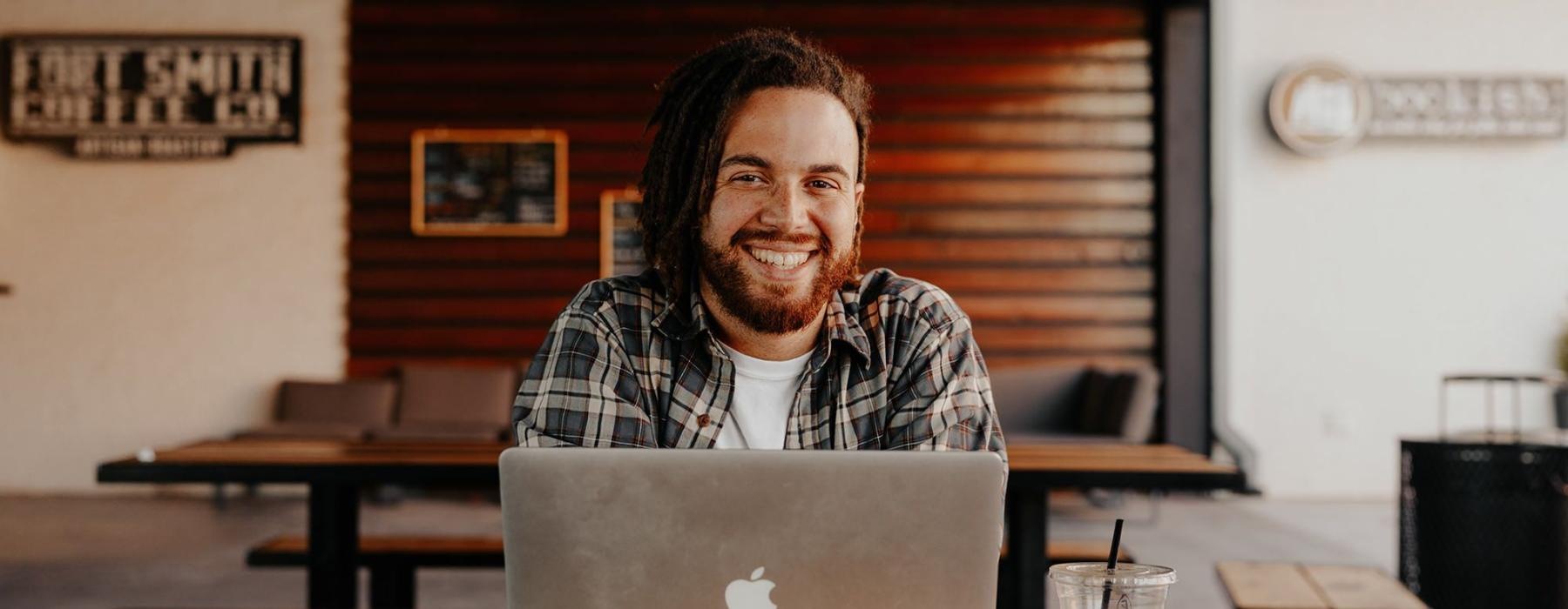 man sits with a drink in front of an open laptop in local restaurant